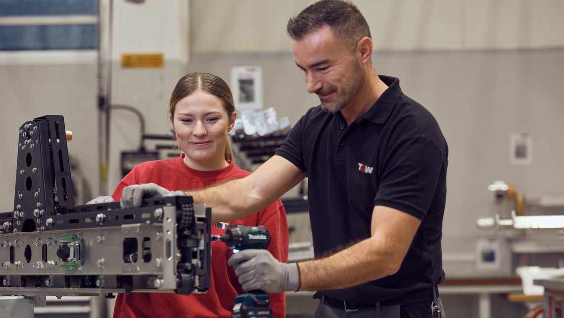 A senior TGW Logistics employee showing how to use a power tool to an apprentice in the training center