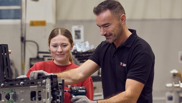 A senior TGW Logistics employee showing how to use a power tool to an apprentice in the training center