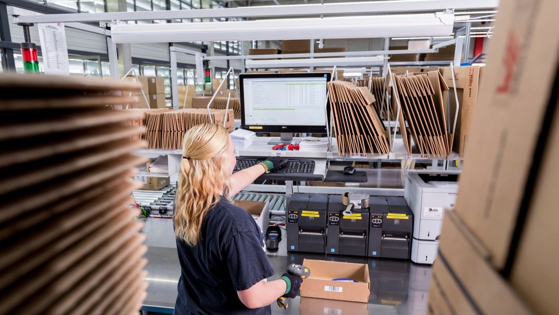 Overview of a blonde woman at a picking station filling a cardboard box