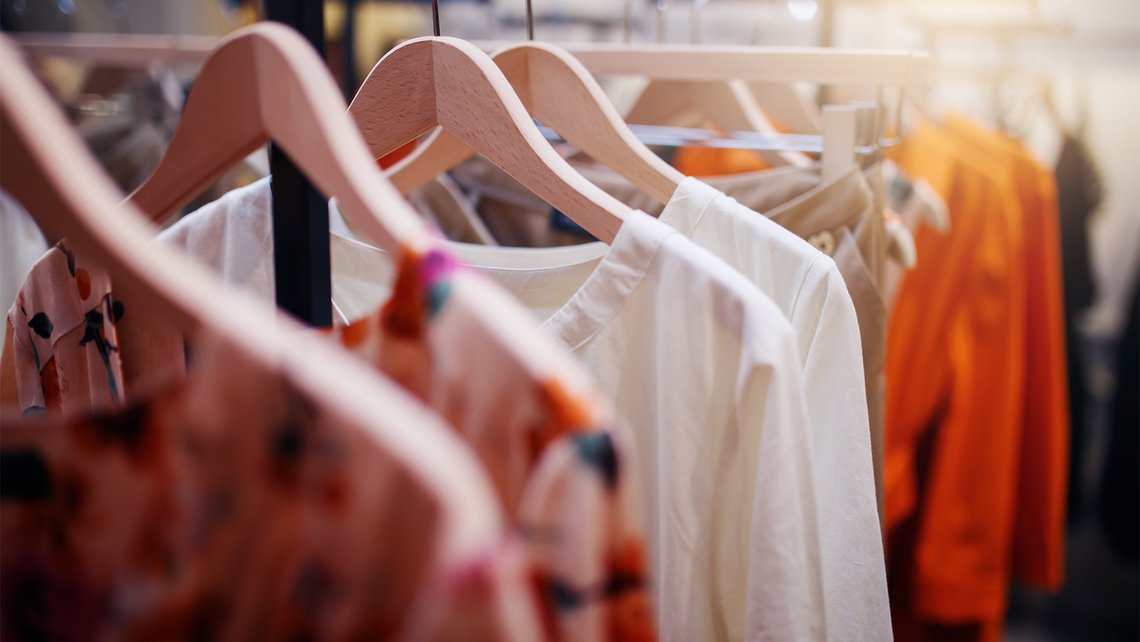 [Translate to Deutsch:] Clothes hang on hangers in a fashion store