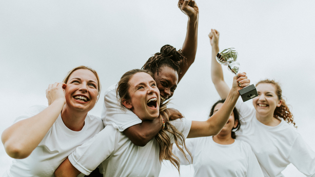 Women's athletic team in white shirts celebrating their victory by raising a trophy