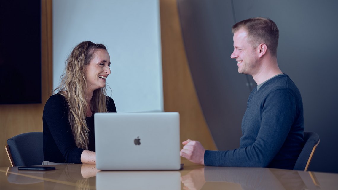 [Translate to France:] A woman and a man talking while sitting in front of a laptop