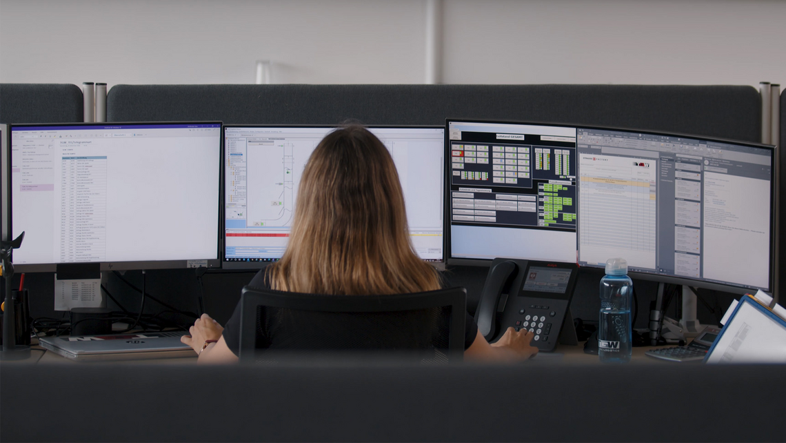 Woman who is monitoring current status of warehouse automation systems at a customer's site on multiple computer screens.