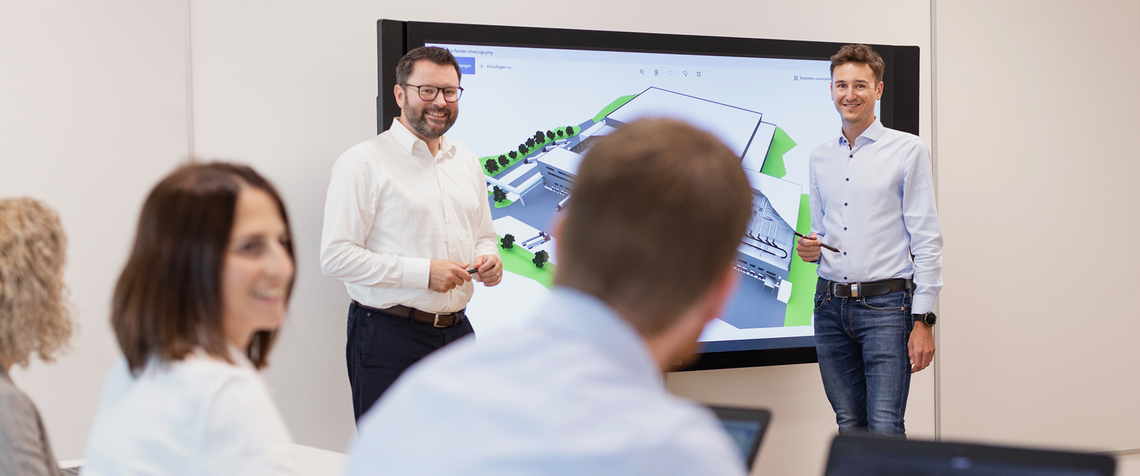 Two people presenting a warehouse automation solution on a large screen to other people