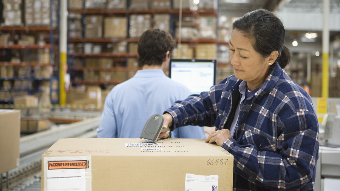 Woman in a warehouse, scanning a label on a carton in her workstation