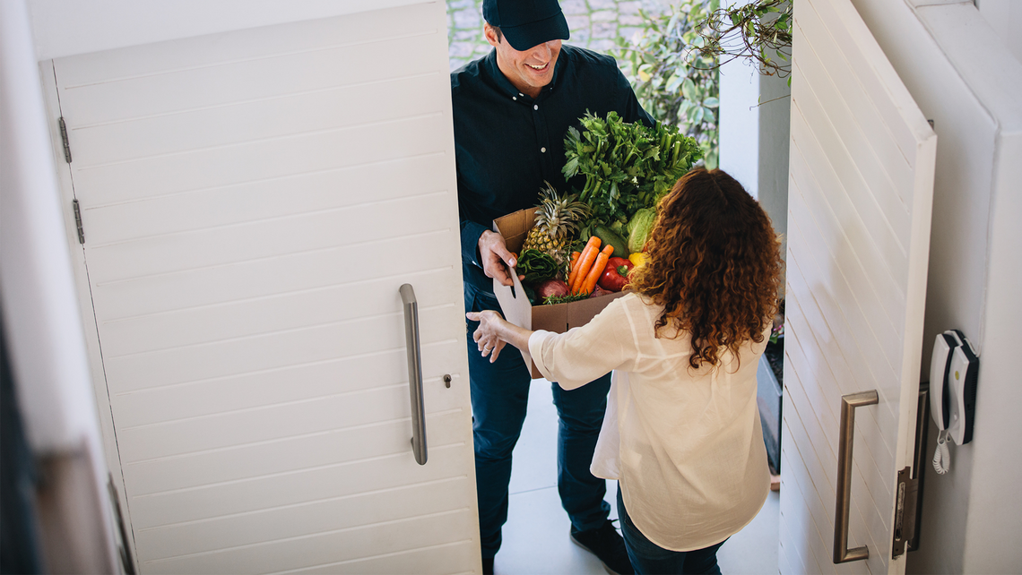 Woman receiving an ecommerce grocery order delivered to her door. Order includes produce.