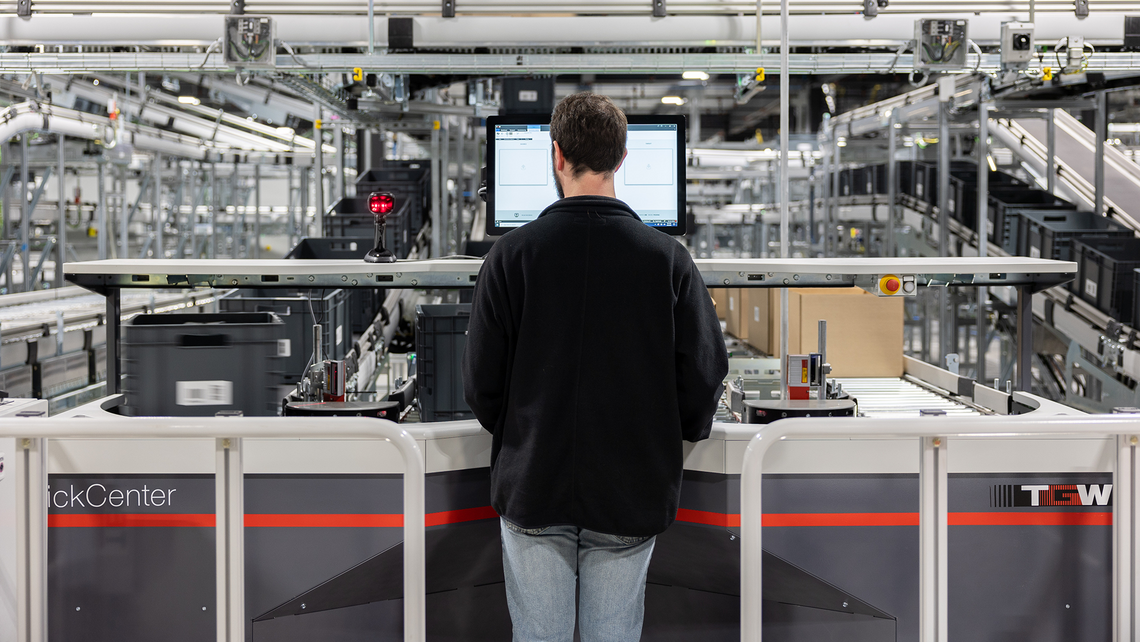 Warehouse worker standing at a TGW Logistics PickCenter One goods-to-person workstation