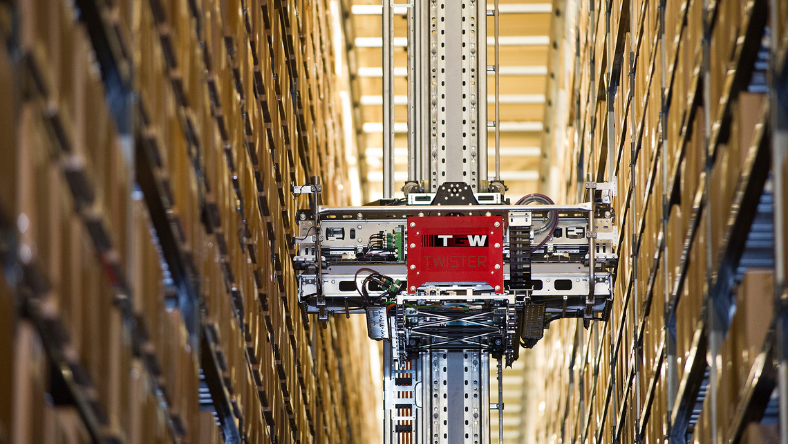 Mini load traveling down an automated storage and retrieval system aisle to grab and transport a carton