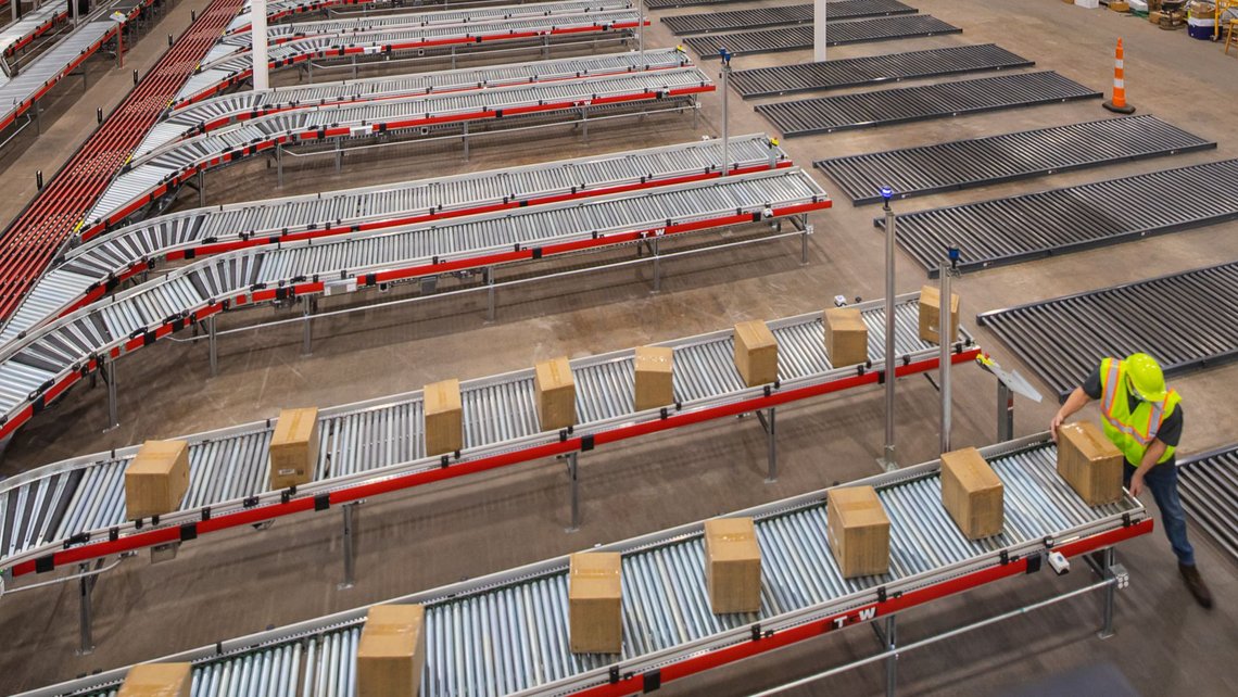 Overview of five conveyor belts next to each other with cardboard boxes in a row and a man picking