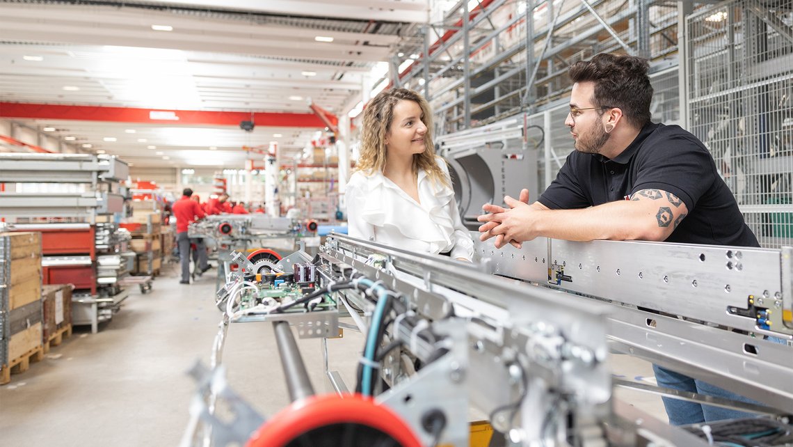 [Translate to North America:] A woman and a man talking in a warehouse area