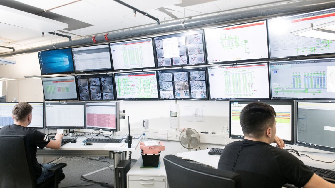 Two persons in front of a large number of screens