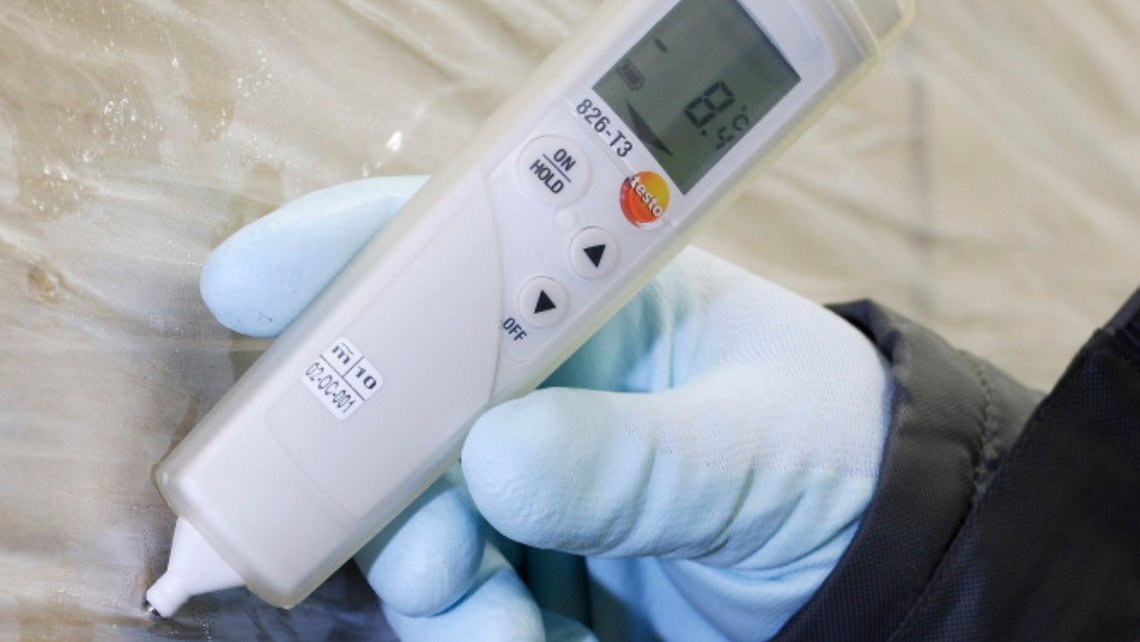 Close-up of a hand holding a temperature gauge on refrigerated goods in a cold storage facility