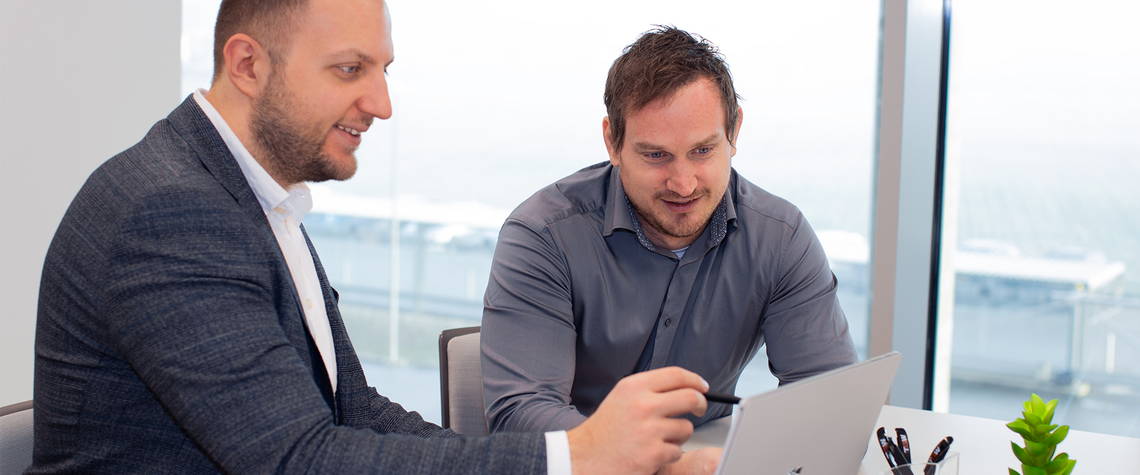 Two men looking at a touchscreen laptop, discussing warehouse automation solutions