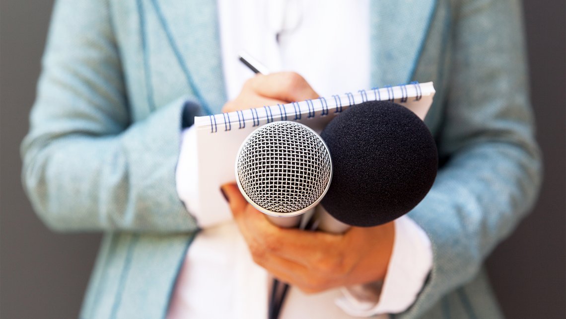 [Translate to Spain:] Close-up of women's hands holding two microphones and a notepad