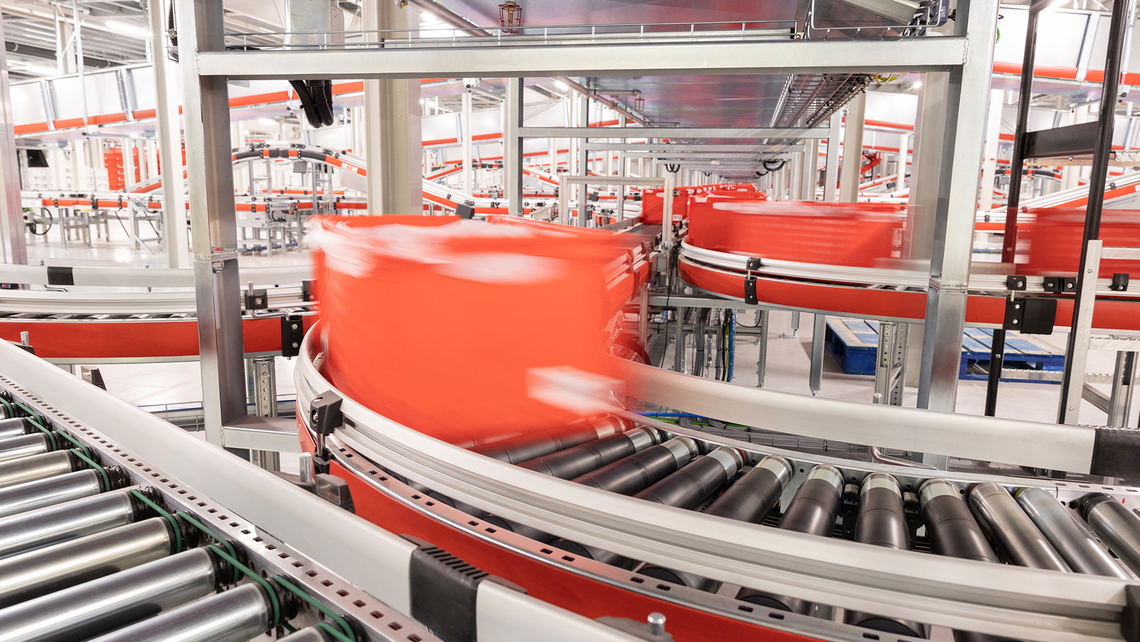 Red totes traveling on multiple conveyor systems throughout the distribution center area