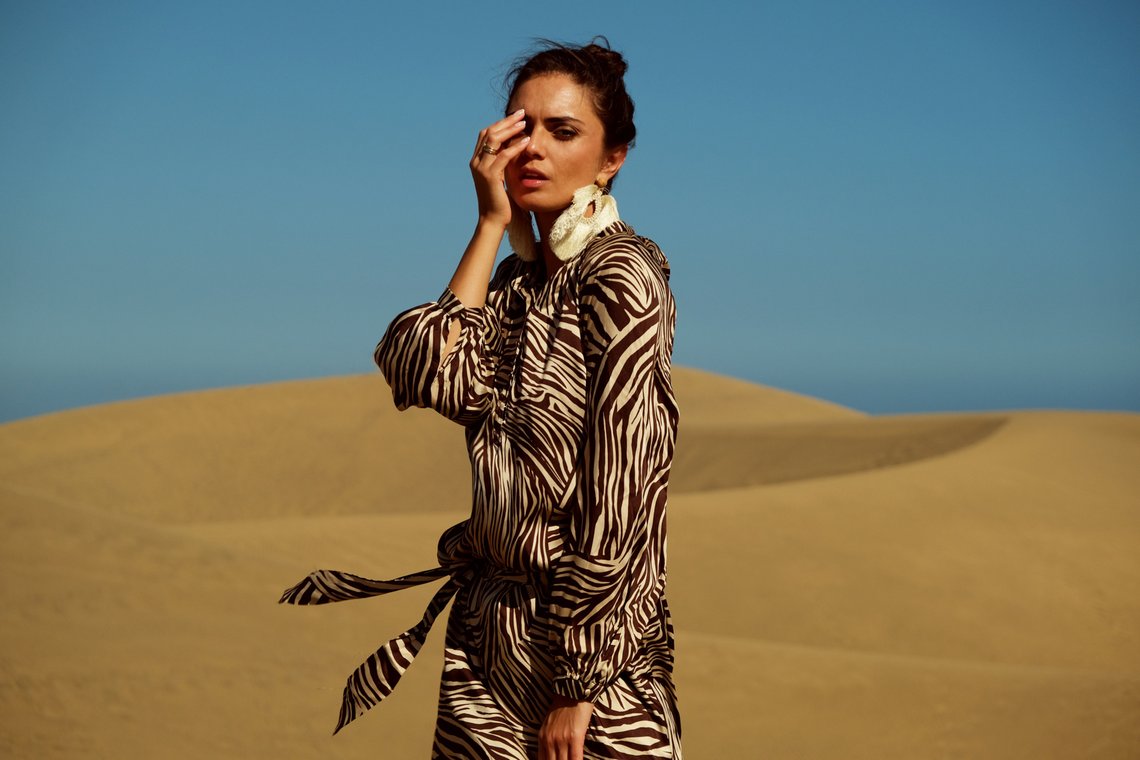 Woman model covering one eye in the desert wearing a panther print dress