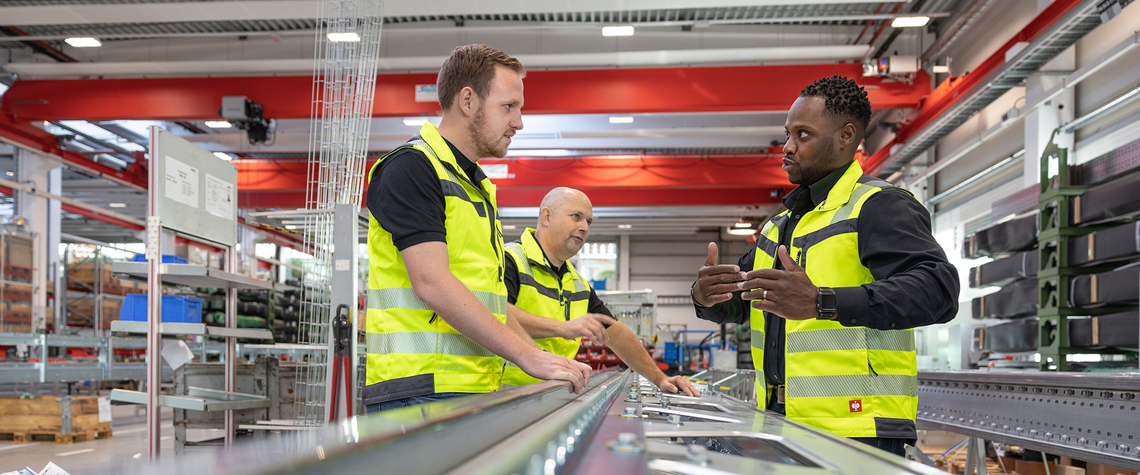 Three men looking closely at some warehouse automation technology, as part of TGW Logistics' training services