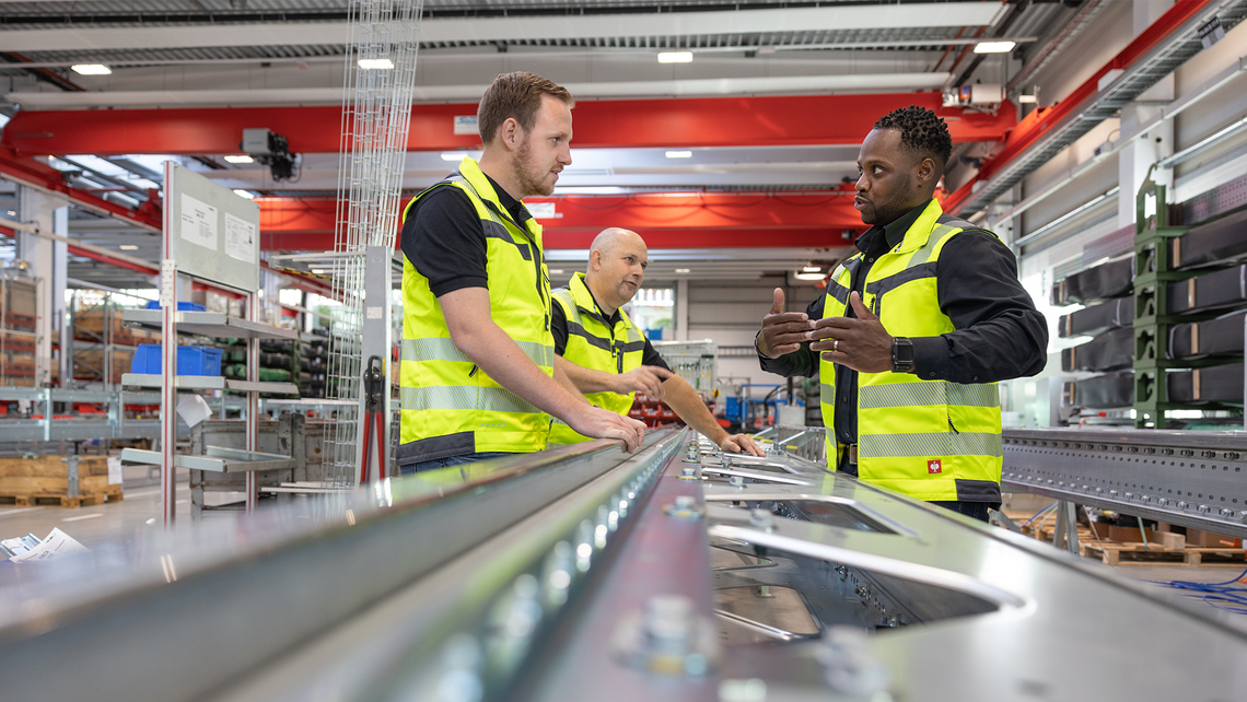 Three men looking closely at some warehouse automation technology, as part of TGW Logistics' training services